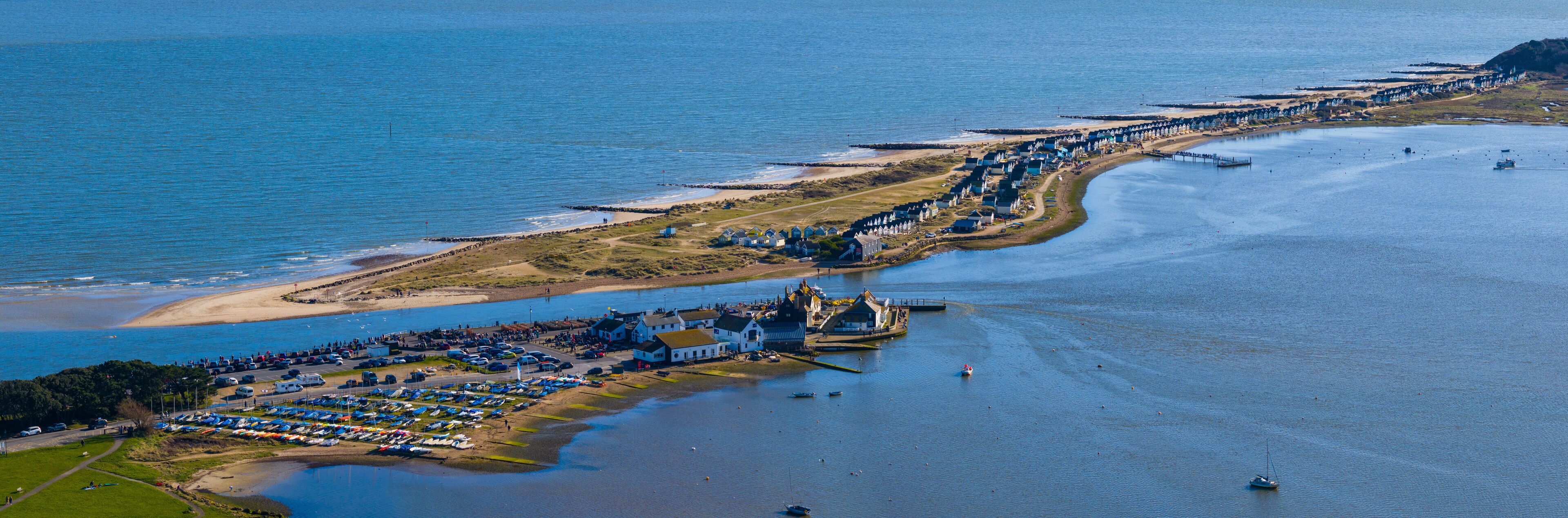 An aerial view of a coastal area with a marina, beach, and row of houses along the shore.