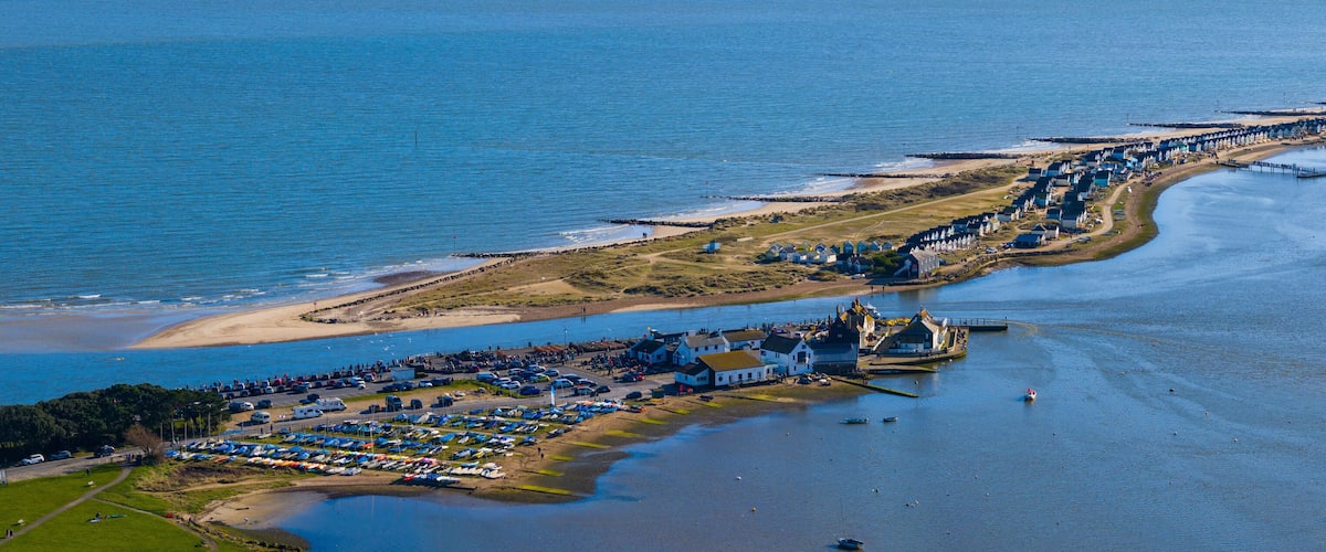 An aerial view of a coastal area with a marina, beach, and row of houses along the shore.