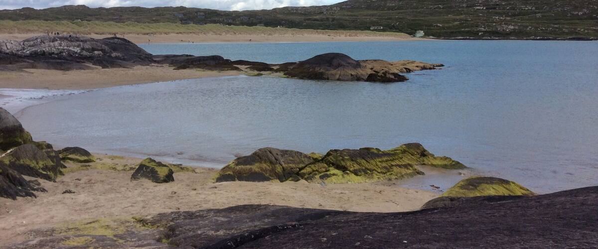 A coastal landscape with rocky shores, a sandy beach, and hills in the background.