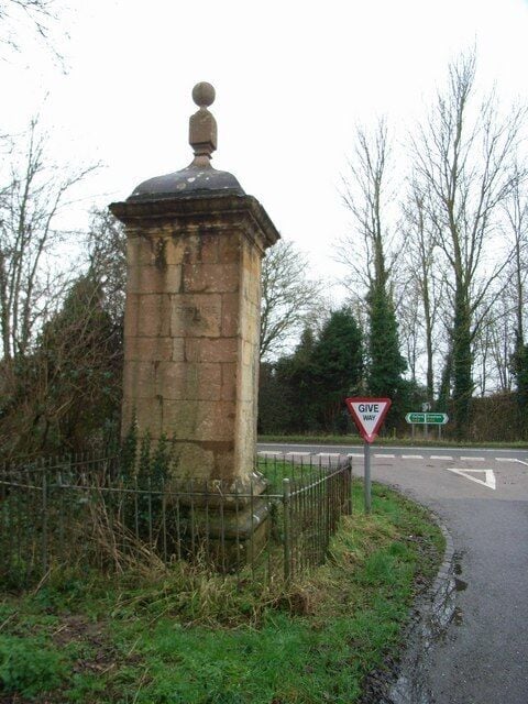 Un monumento de piedra con una cúpula y una parte superior esférica, una señal de tráfico que indica 'Ceda el Paso' y una señal de carretera direccional.