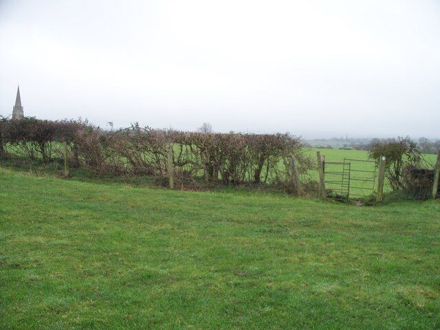 A rural landscape with a grassy field, a wooden fence, and a distant church spire.