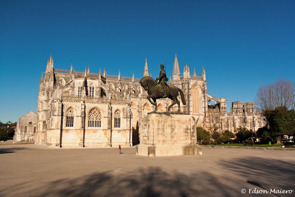 Una catedral histórica con arquitectura gótica, una estatua de una figura a caballo y un cielo azul despejado.
