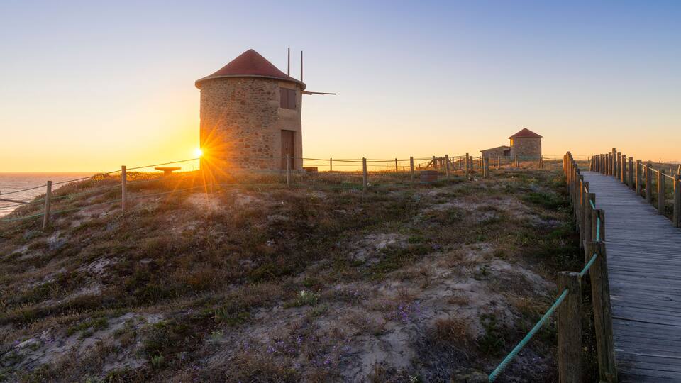 A coastal landscape with a stone tower and a wooden walkway leading to a smaller structure.