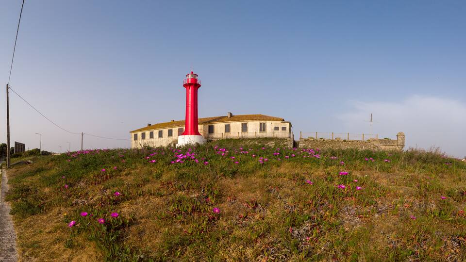 A red lighthouse on a grassy hill with a building in the background.