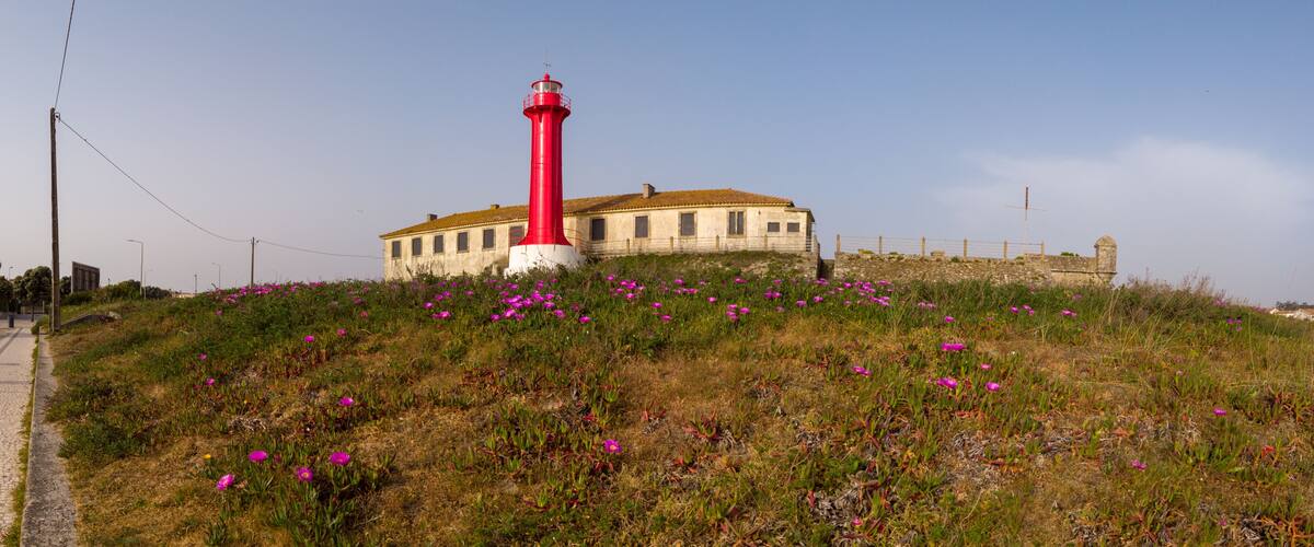 A red lighthouse on a grassy hill with a building in the background.