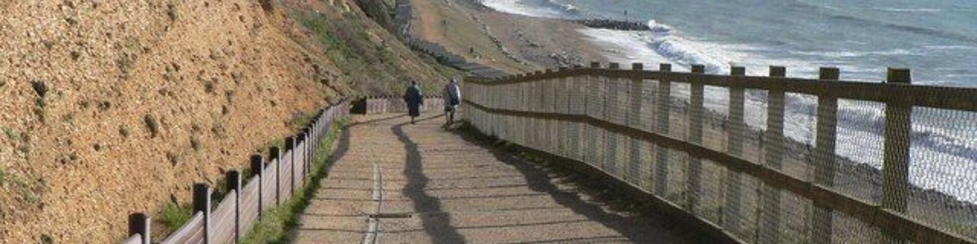 Un paseo marítimo con valla de madera, un risco rocoso y el océano al fondo.