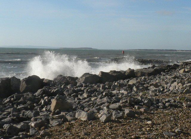 A rocky shoreline with waves crashing against the rocks and a red buoy in the distance.
