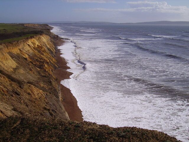 A coastal cliff with a beach and ocean waves.