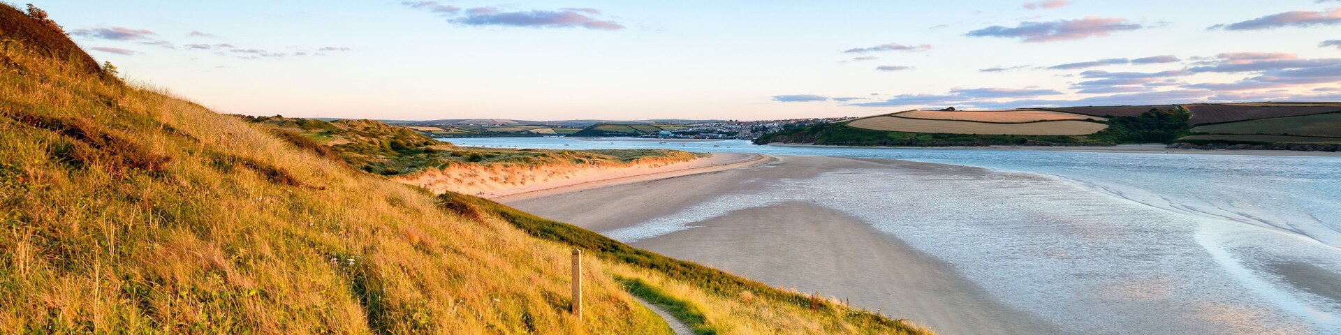 A coastal landscape with a sandy beach, grassy hills, and a clear sky.
