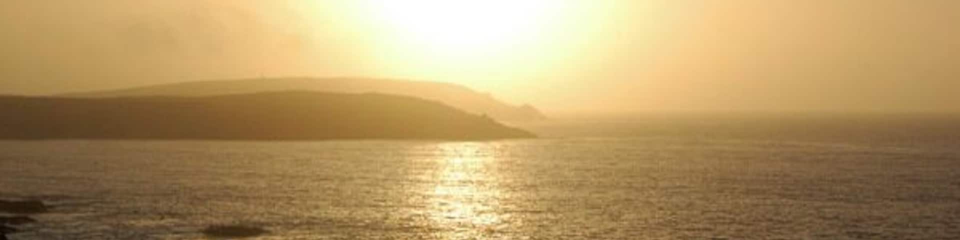 Un atardecer sobre un mar en calma con tierra a lo lejos.
