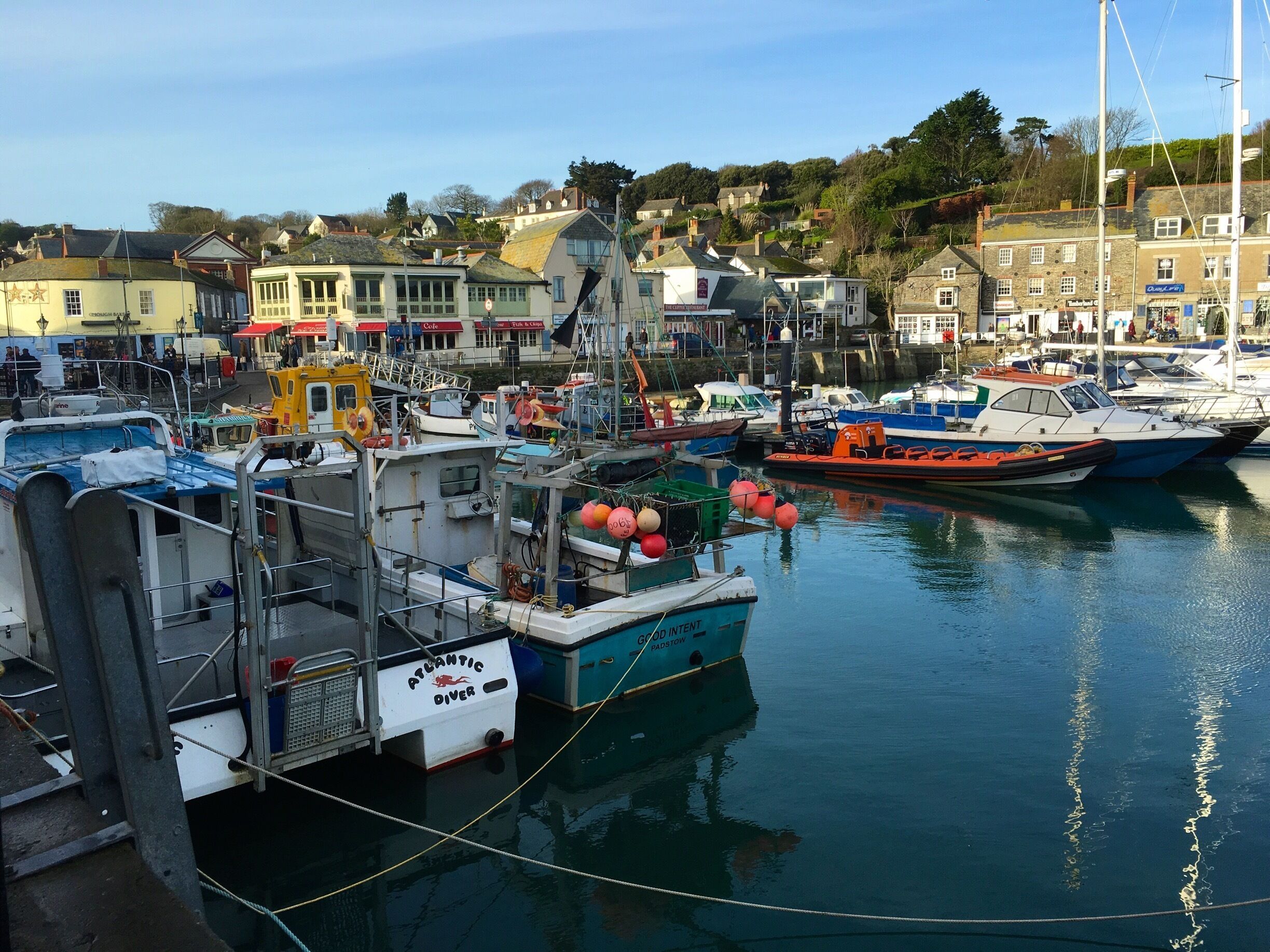 A marina with various boats docked, a lifeboat, and buildings in the background.