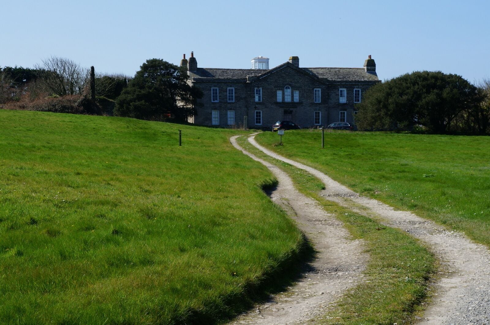 A grassy field with a dirt path leading to a stone building.