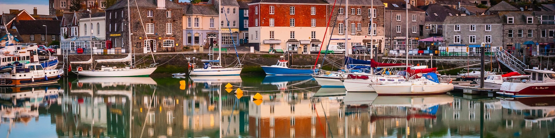 Un puerto con barcos amarrados, edificios a lo largo del muelle y un reflejo claro en el agua.