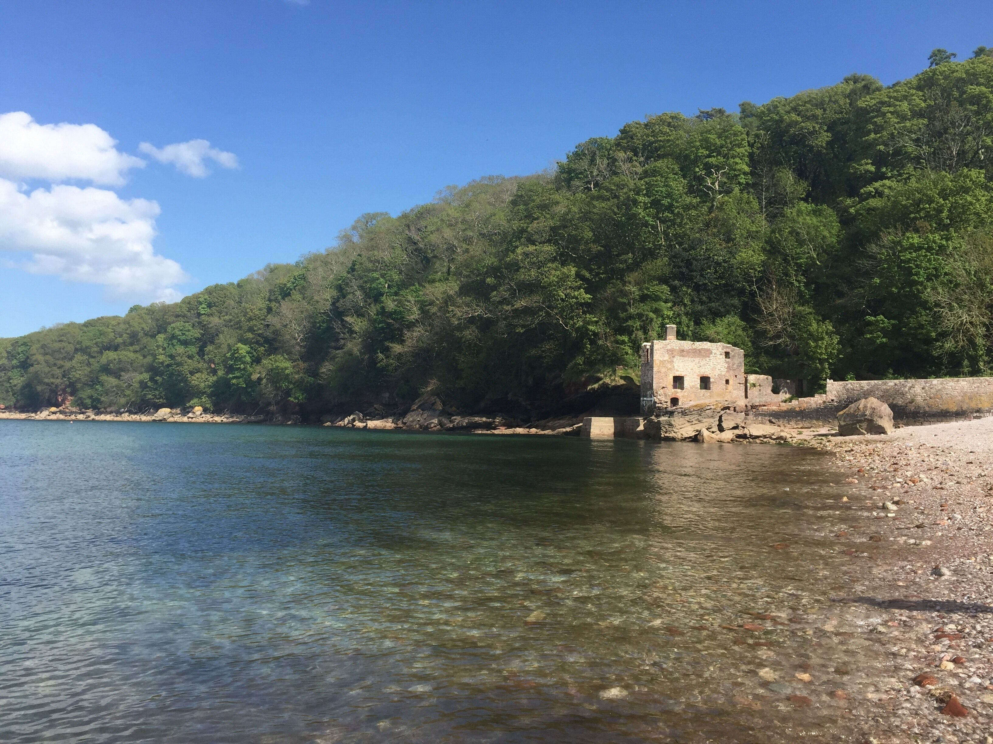 A clear lake with a stone structure on the shore, surrounded by dense forest.