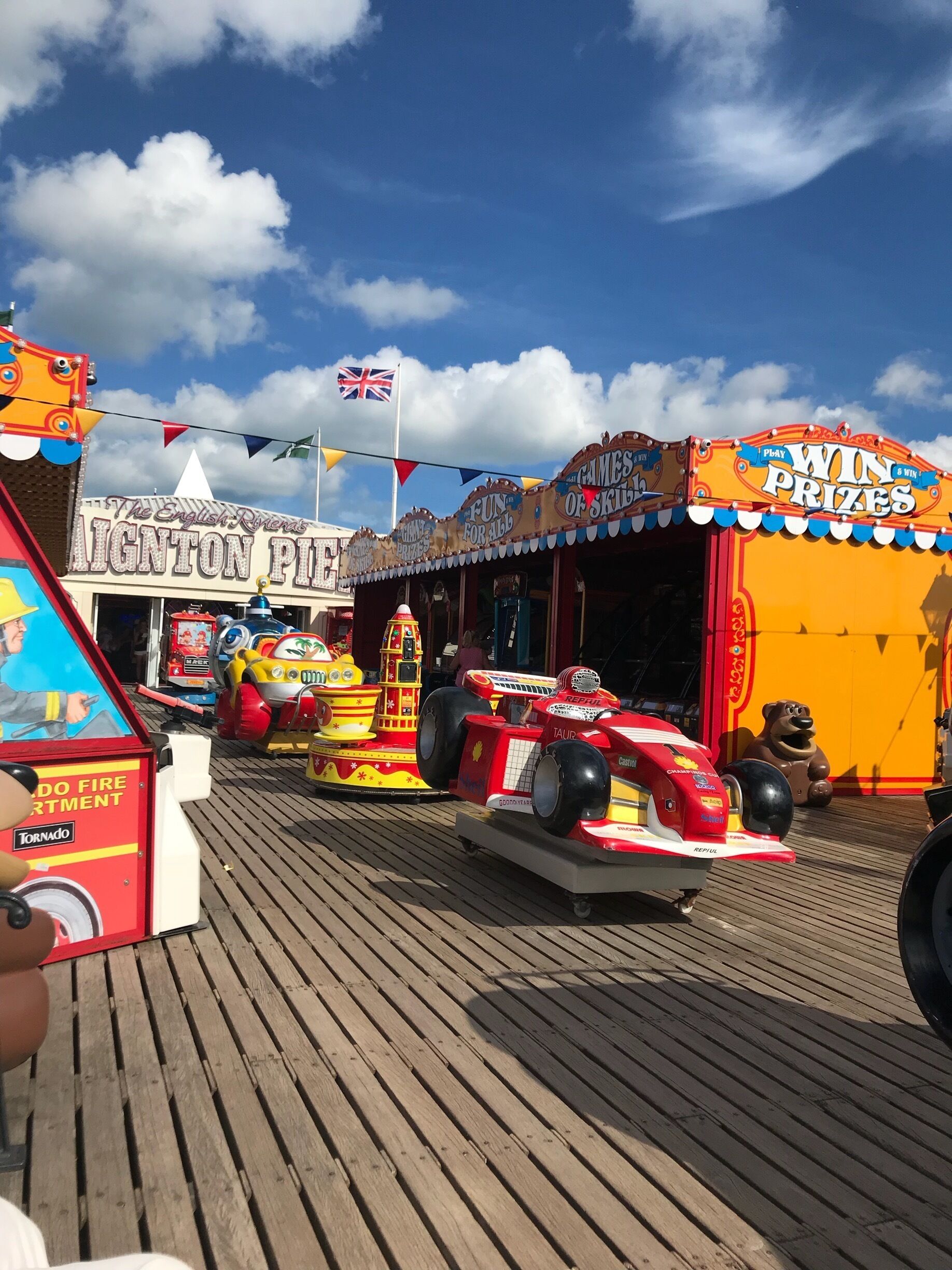 A wooden boardwalk with various amusement rides, including a fire truck and a racing car.