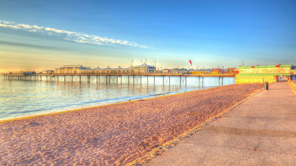 A beach with a pier extending into the water, a boardwalk, and a colorful building.