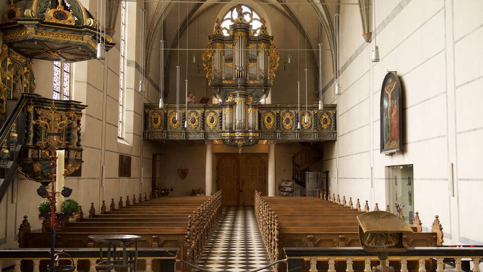 An ornate church interior with a checkered floor, pews, and a large organ.