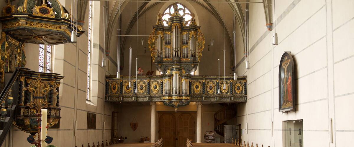 An ornate church interior with a checkered floor, pews, and a large organ.