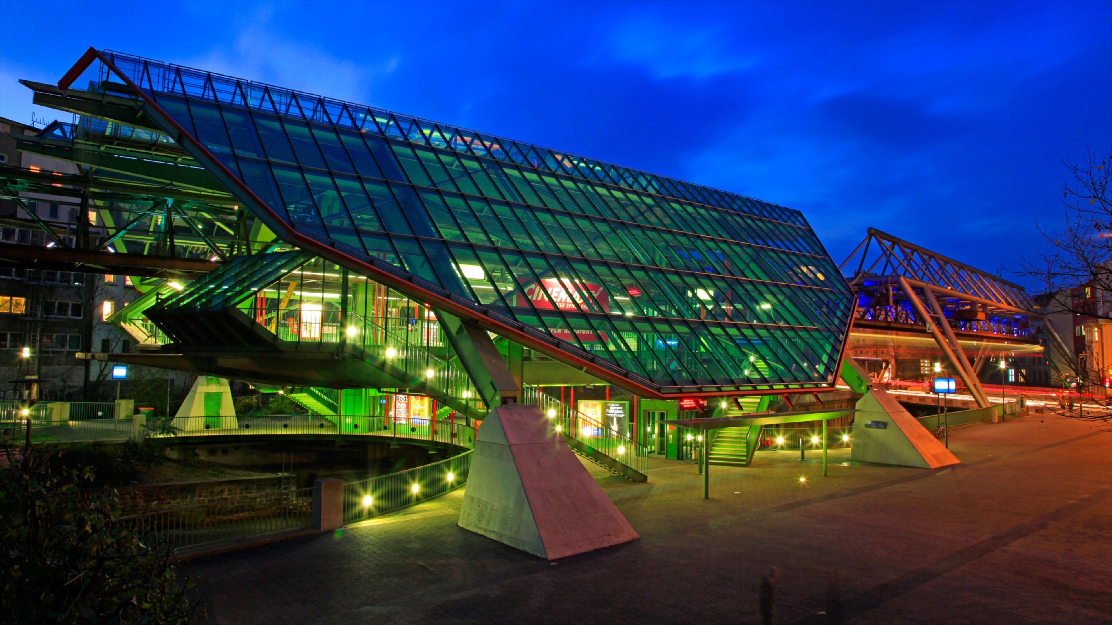 A modern glass building with a green roof and a ramp leading up to it.