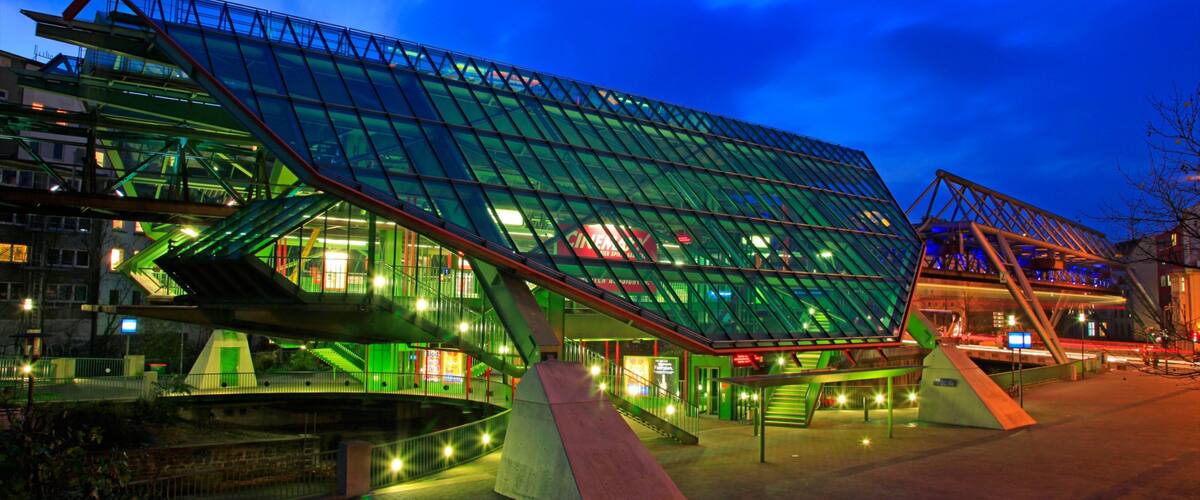 A modern glass building with a green roof and a ramp leading up to it.