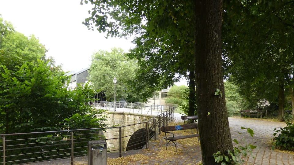 A stone bridge, a metal fence, a bench, and a tree in a park.