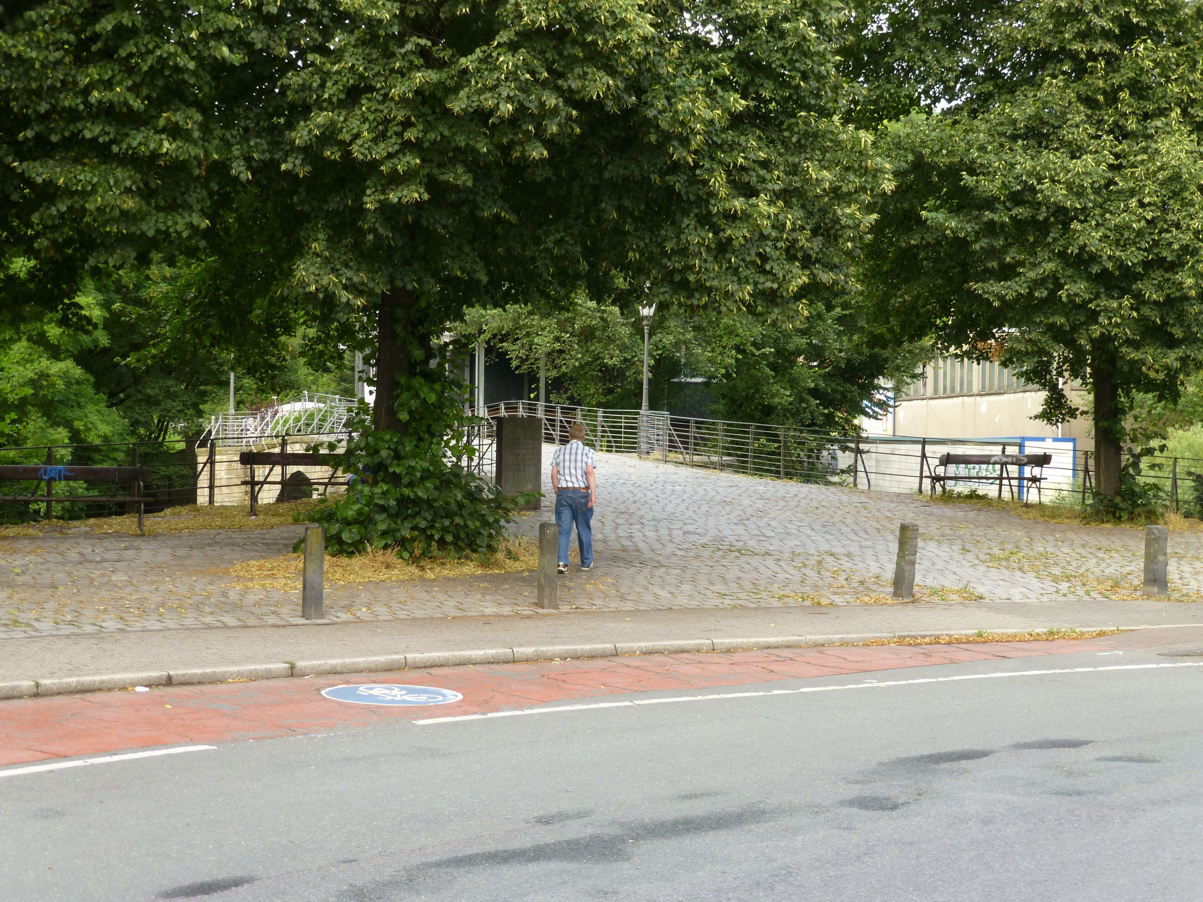A paved pathway with a bicycle lane, trees, a fence, and a bench.