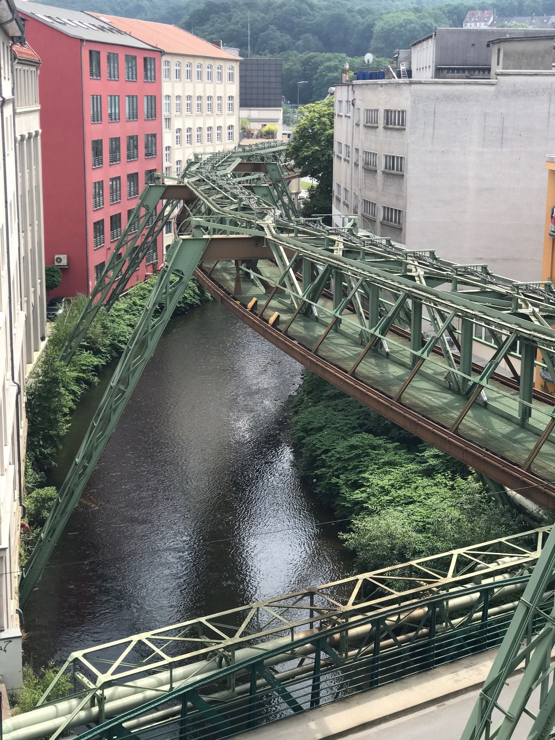 A green metal bridge over a river with buildings on either side.