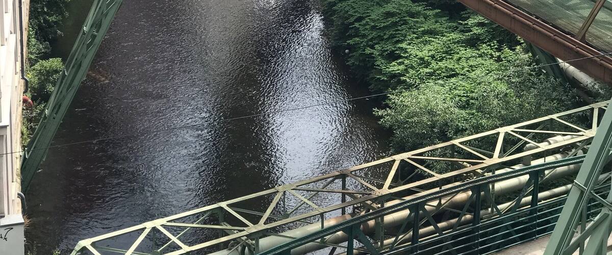 A green metal bridge over a river with buildings on either side.