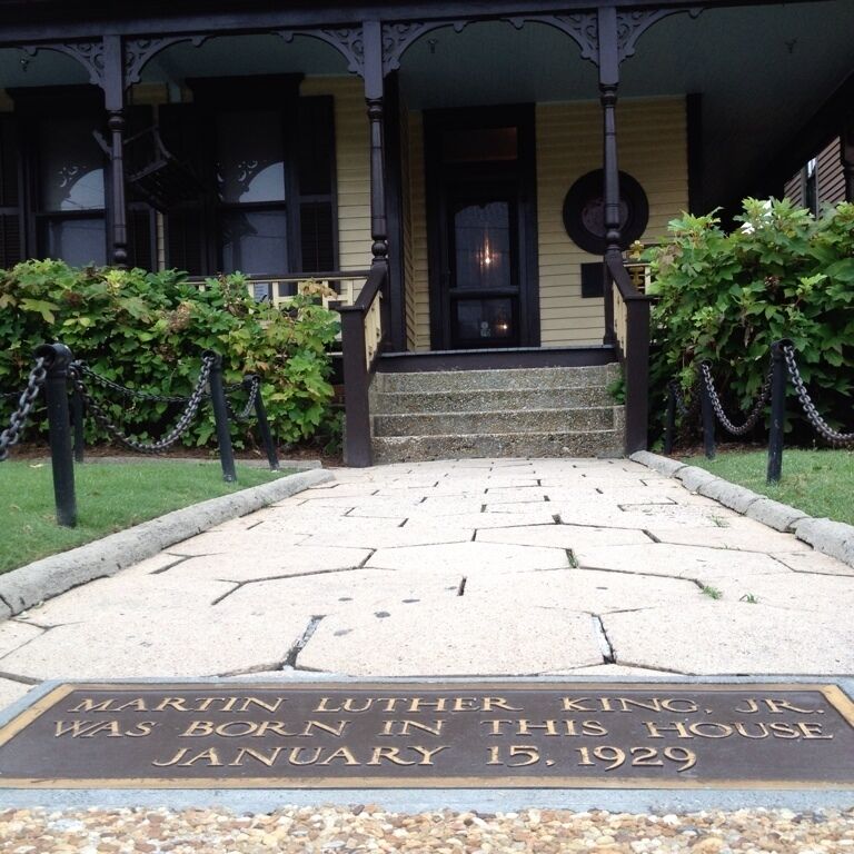 A historical plaque at the entrance of a house with a porch, surrounded by greenery.