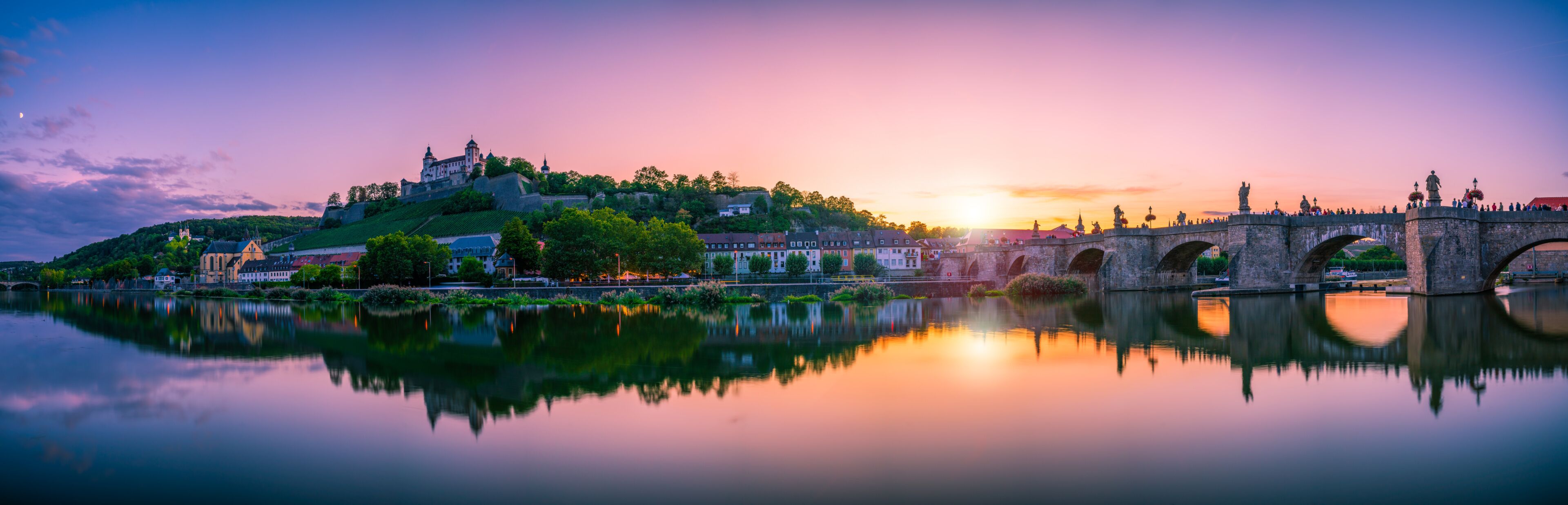 Atardecer sobre un río con un puente y un castillo en una colina.