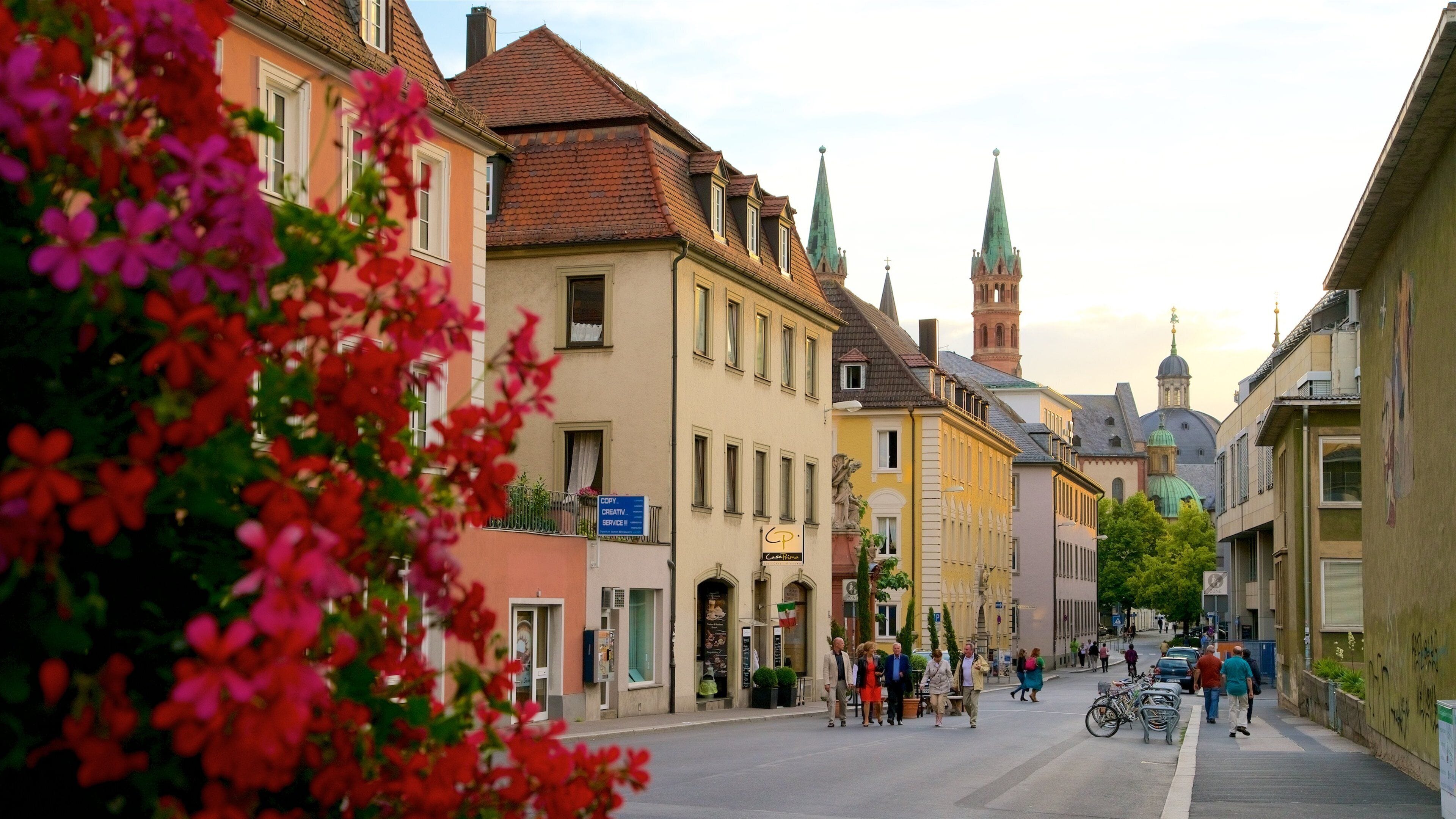 A street with historic buildings, a church spire, and people walking.