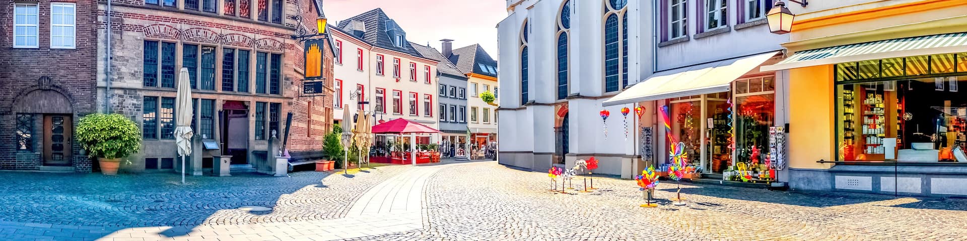 A cobblestone street lined with historic buildings, a church tower, and a colorful sunset sky.