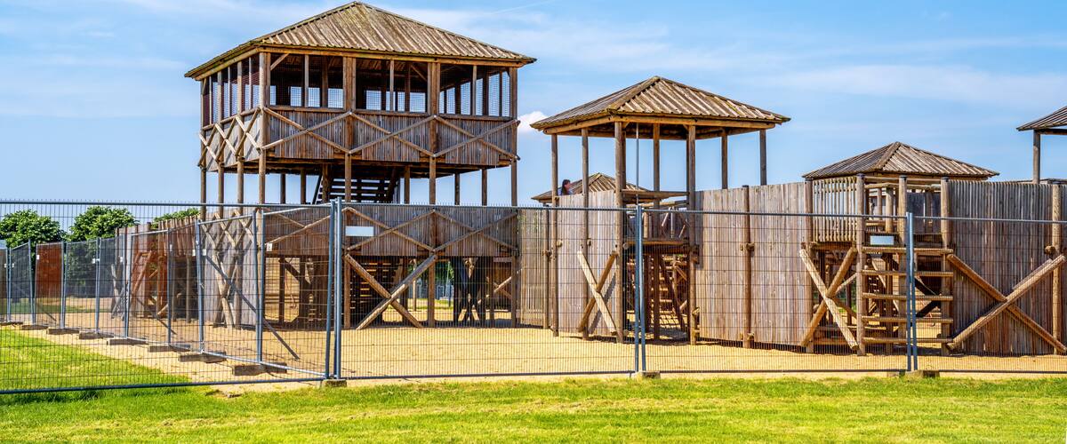 A fenced playground with wooden climbing structures and a clear blue sky.