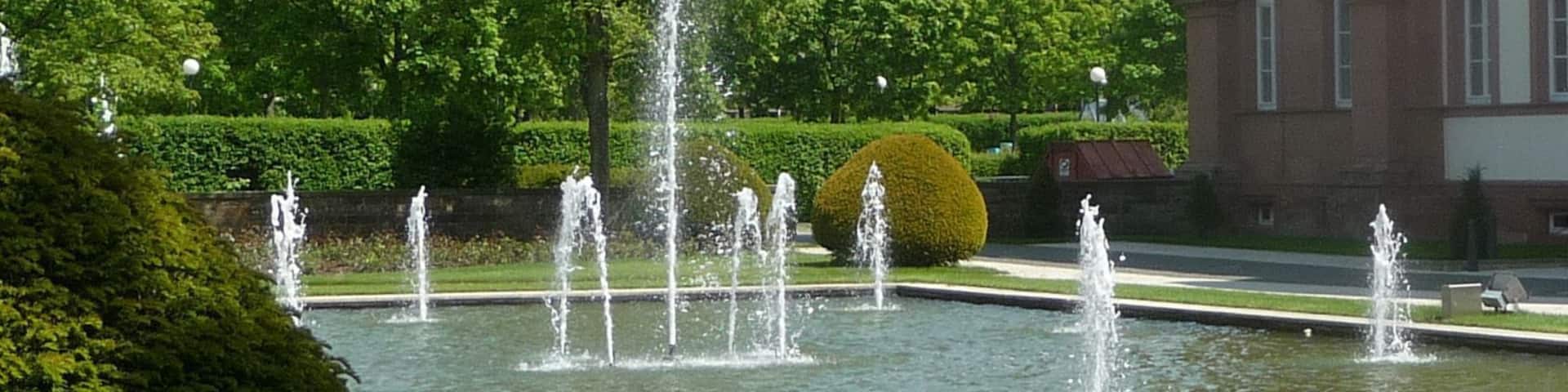 A fountain in a park with a building in the background.