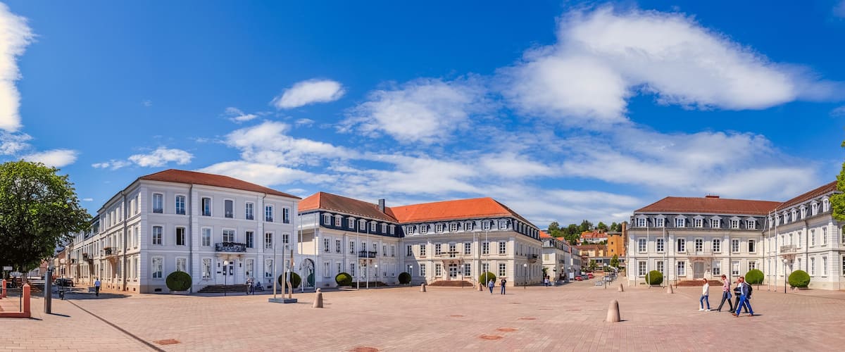A historic square with classical architecture, cobblestone pavement, and a statue.