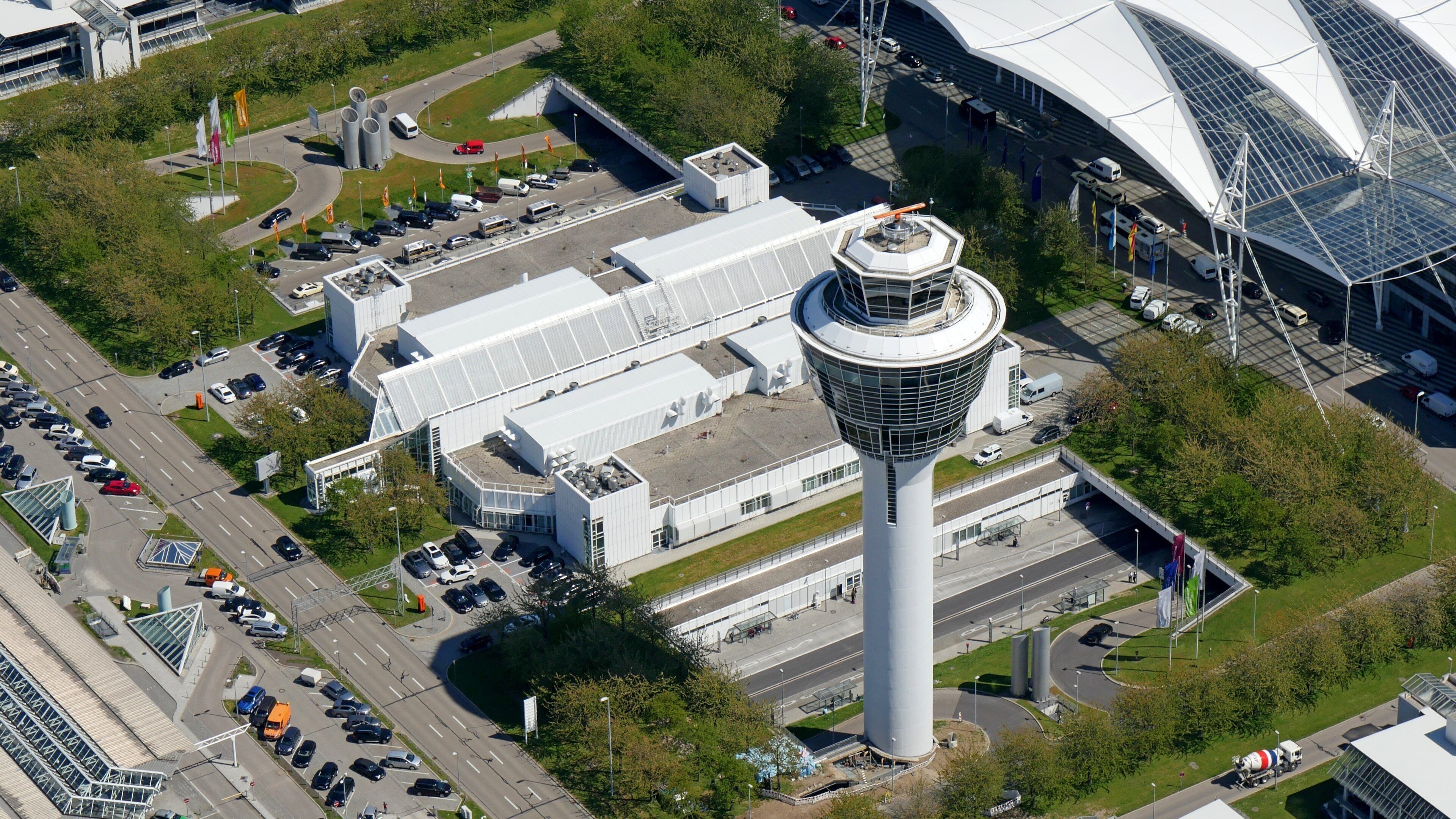 An aerial view of a modern industrial complex with a prominent tower, parking areas, and a large stadium.