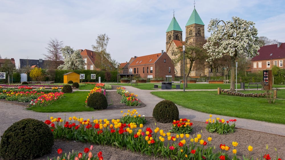 Une église aux flèches vertes, un jardin fleuri et un chemin pavé.