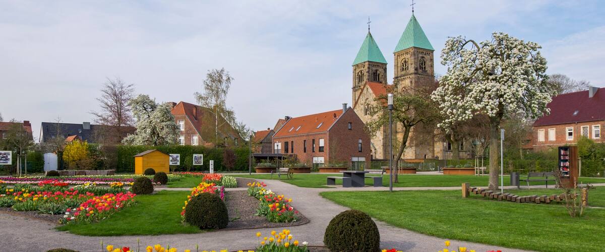 A church with green spires, a flower garden, and a paved walkway.
