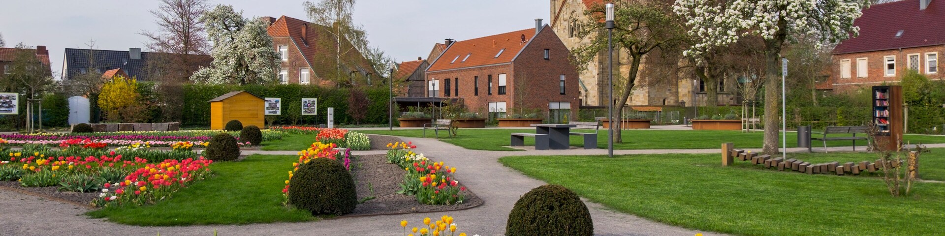 A church with green spires, a flower garden, and a paved walkway.