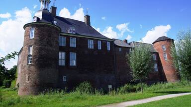 A large brick building with a tower and a smaller brick tower, surrounded by greenery.