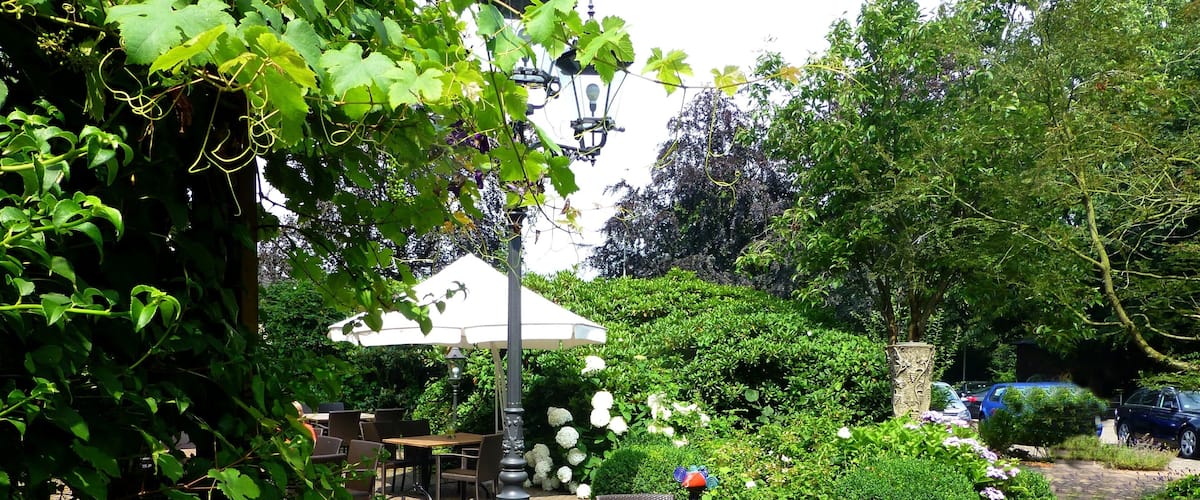 An outdoor cafe with stone flooring, wicker chairs, and a table under a white umbrella.