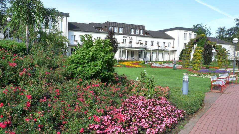 A hotel surrounded by a well-maintained garden with various flowers and shrubs.