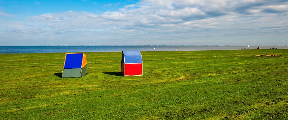Two colorful beach umbrellas on a grassy field with a view of the sea and distant wind turbines.
