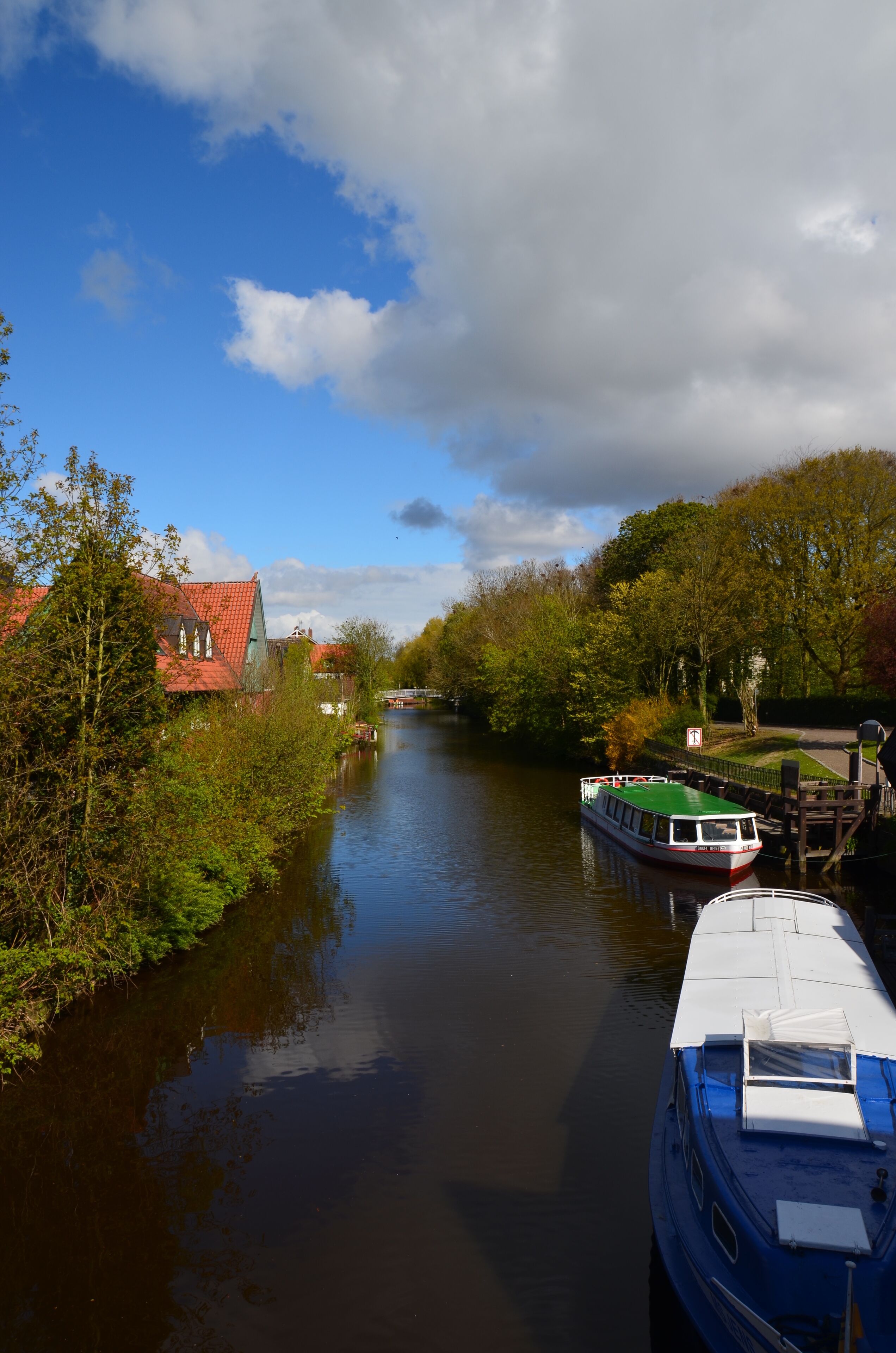 A narrow river with boats, a red-roofed building, and green trees.