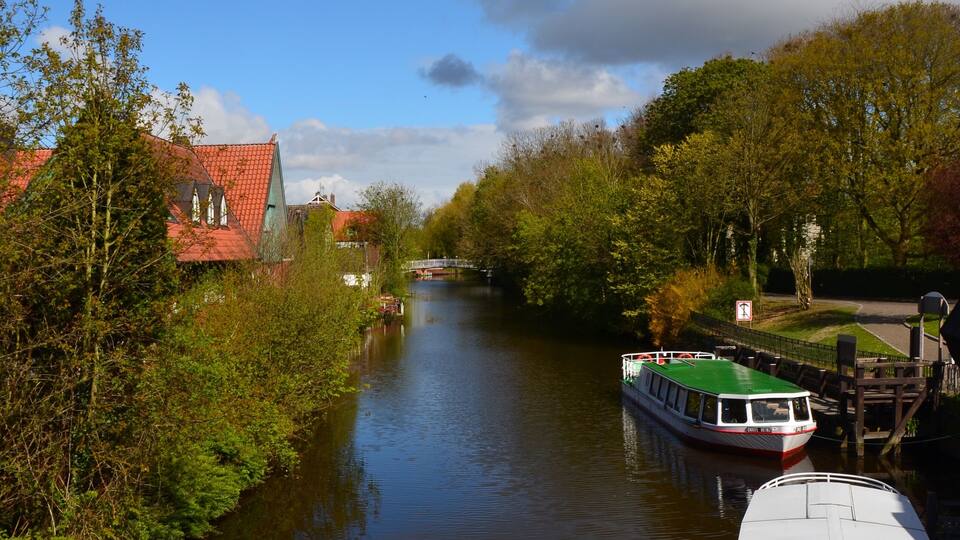 A narrow river with boats, a red-roofed building, and green trees.