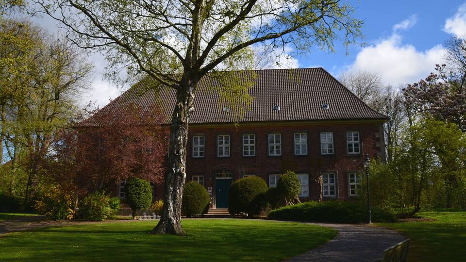 A red brick building with a tiled roof, surrounded by green grass and trees.