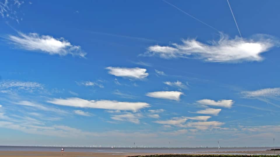 A beach with a clear sky, distant city skyline, and a rocky outcrop.