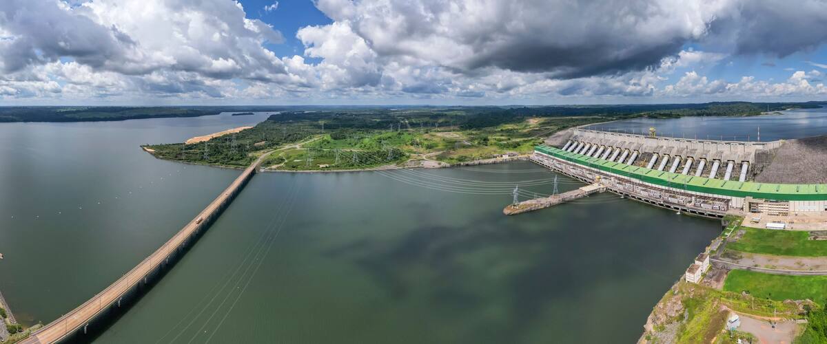 A large dam with multiple turbines, a long bridge, and surrounding greenery.