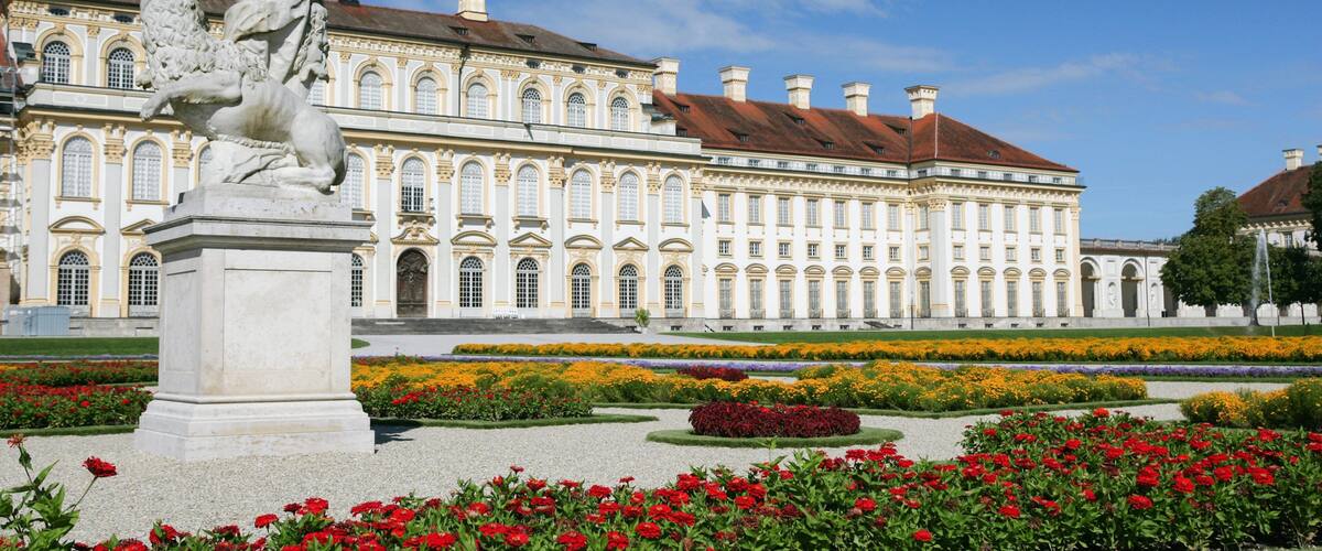A classical statue in a garden with a large ornate building in the background.