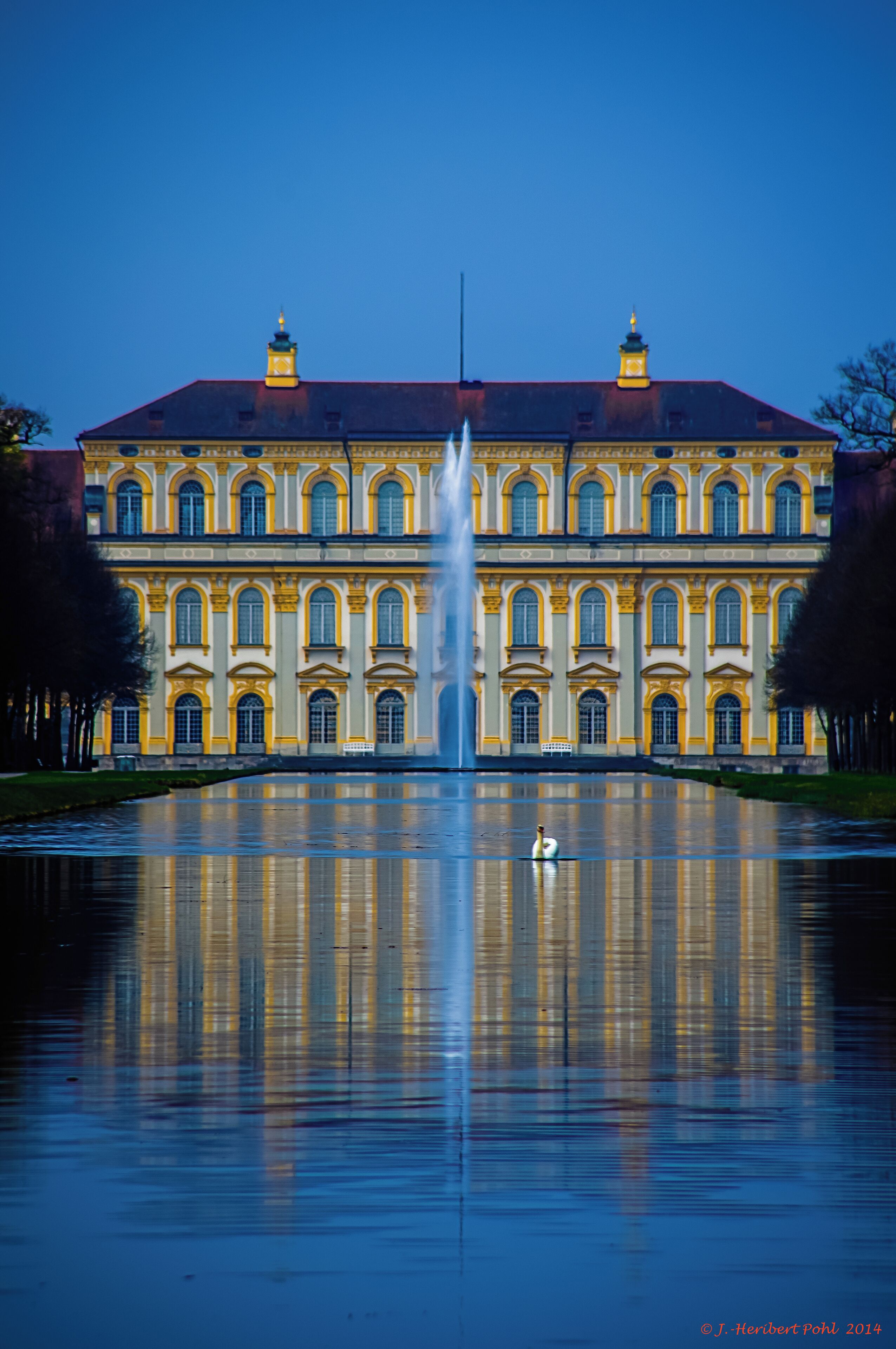 A large yellow building with a fountain in front.